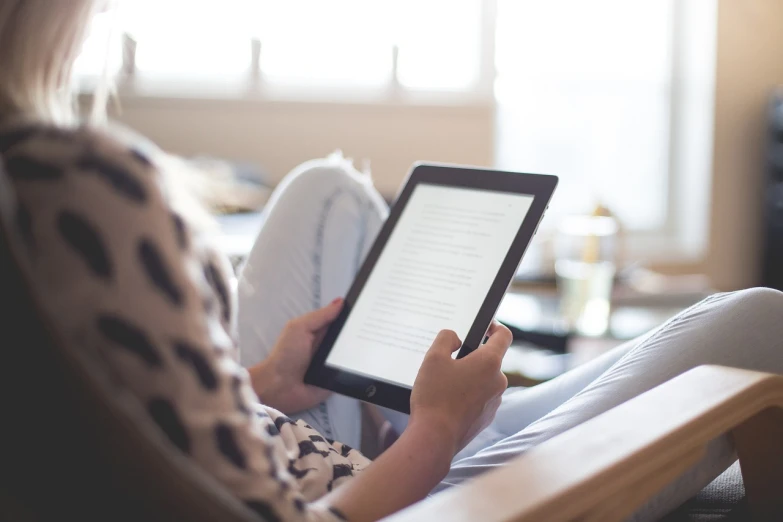 a woman sitting in a chair reading a book, pixabay, took on ipad, slightly blurred, advert, pictured from the shoulders up