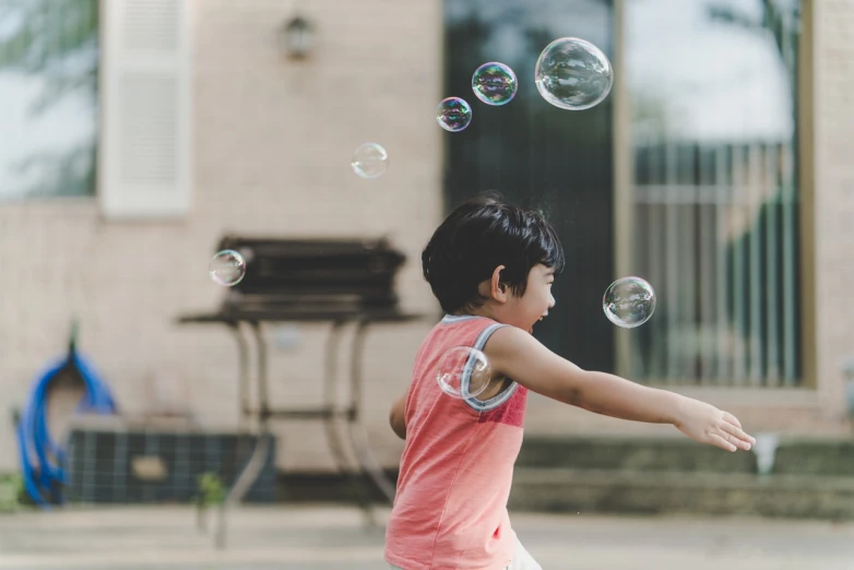 a young boy is playing with soap bubbles, a picture, shutterstock, side view of her taking steps, shot in canon 50mm f/1.2, young asian girl, his arms spread. ready to fly