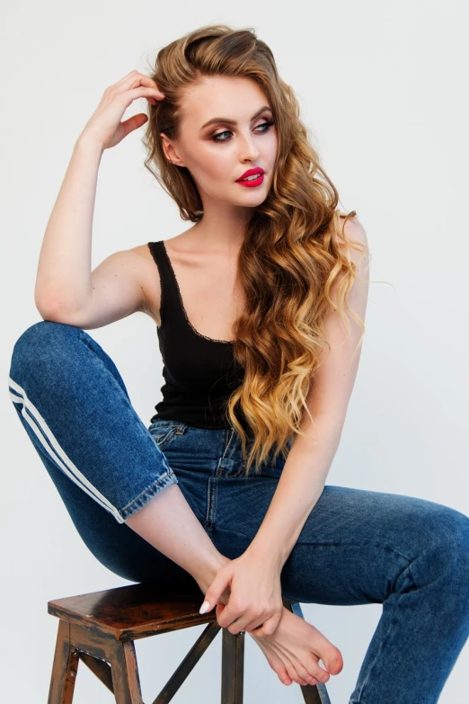 a woman sitting on top of a wooden stool, a portrait, inspired by Ksenia Milicevic, tumblr, arabesque, tight denim jeans, big red lips, glamorous hairstyle, wearing a cropped black tank top