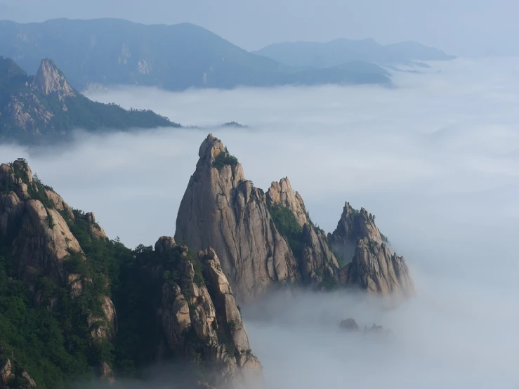 a plane that is flying over some mountains, a picture, by Yi Jaegwan, fog fills the area, tall stone spires, wikimedia commons, seoul