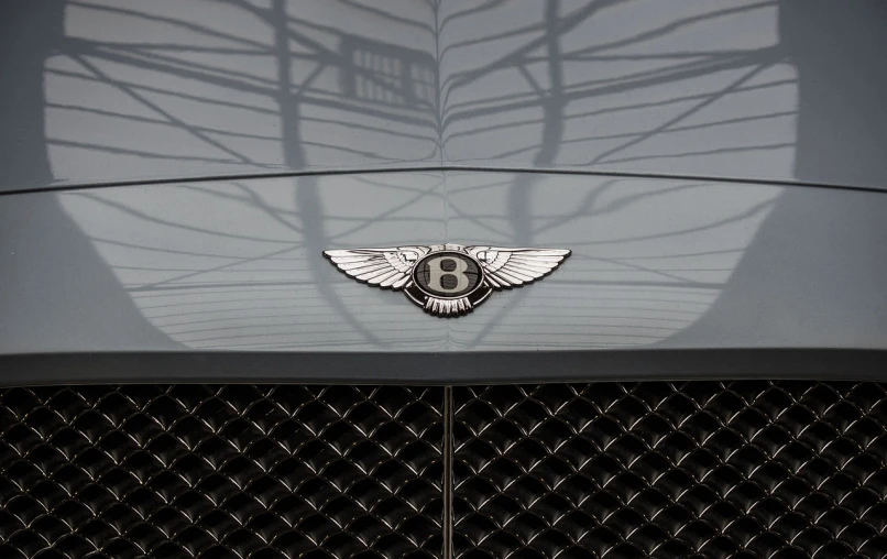 a bentley logo on the front of a car, a portrait, by Austin English, gun metal grey, detailed 85mm f/1.4, with two pairs of wings, ultrafine detail ”