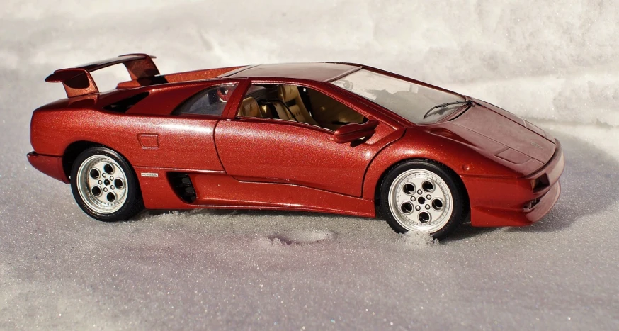 a red toy car sitting on top of a snow covered ground, a macro photograph, inspired by Dahlov Ipcar, pantera ((countach)), hyperdetailed!!, brushed rose gold car paint, high detailed wheels