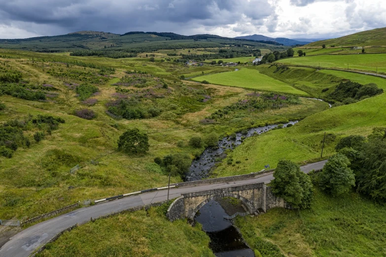 a train traveling over a bridge over a lush green valley, a portrait, by John Murdoch, flickr, small flowing stream from wall, drone wide shot, moorland, shepherd's crook