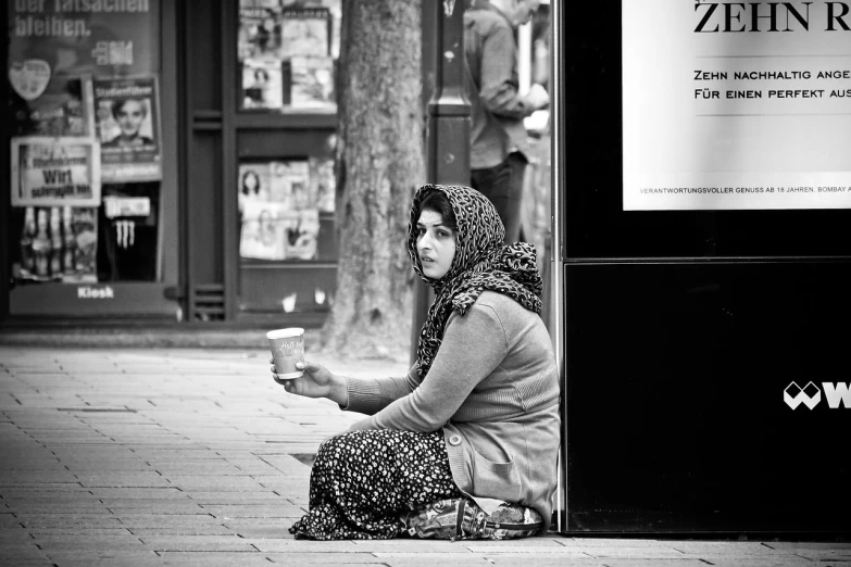 a black and white photo of a woman sitting on the sidewalk, a photo, by Etienne Delessert, featured on pixabay, muslim, worst place to live in europe, drinking a coffee, people waiting in bus stop