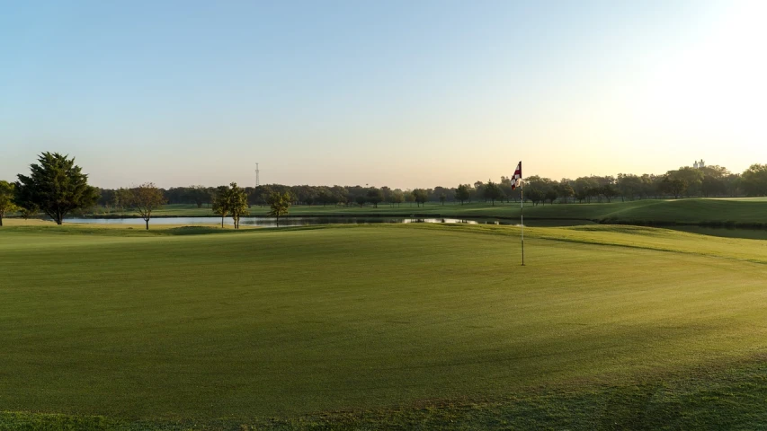 a green golf course with a lake in the distance, by Scott M. Fischer, early morning sunrise, texas, b - roll, high res photo