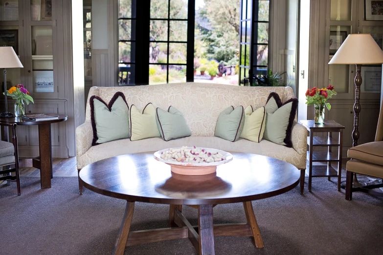 a living room filled with furniture and a cake on top of a table, by William Home Lizars, pixabay, light beige pillows, round doors, soft green natural light, sitting on a mocha-colored table