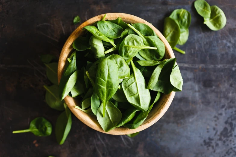 a wooden bowl filled with spinach leaves, shutterstock, on a dark background, 💣 💥, profile pic, 1 6 x 1 6