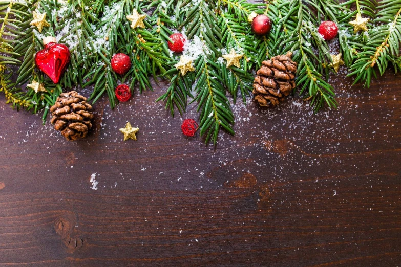 a wooden table topped with pine cones and christmas decorations, pexels, folk art, snowflakes falling, background image, evergreen branches, wallpaper - 1 0 2 4