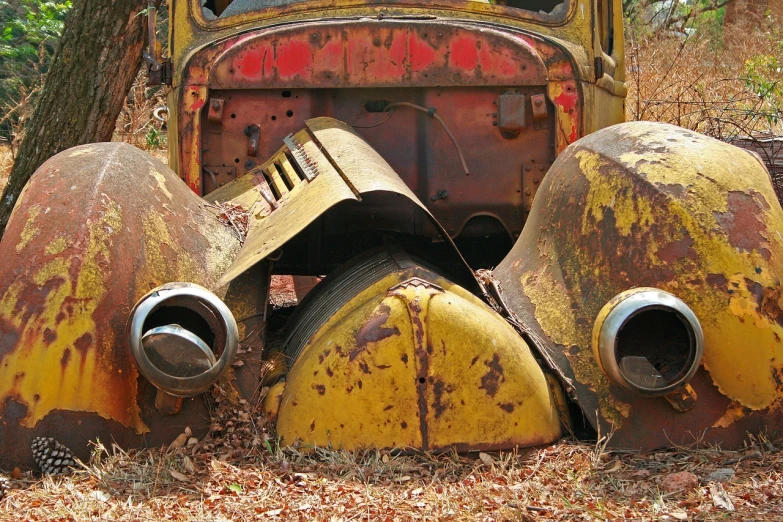 an old rusted truck sitting in the woods, by Tom Carapic, flickr, assemblage, yellow and red, burned cars, middle close up composition, yellow helmet