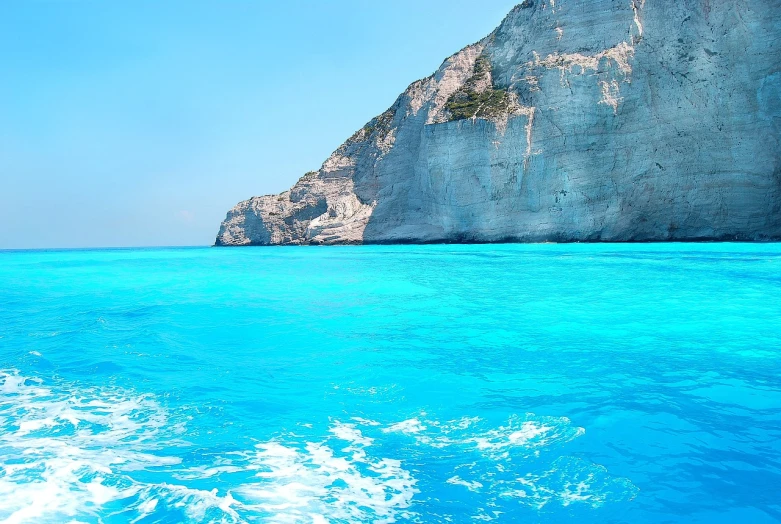 a body of water with a cliff in the background, a picture, by Alexis Grimou, shutterstock, blue and cyan colors, vacation photo, very very well detailed image, stock photo