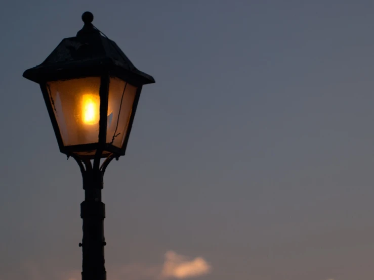 a street light with the sun setting behind it, a picture, by Jan Rustem, shutterstock, realism, one single gas lamp, night time footage, close establishing shot, yellow artificial lighting