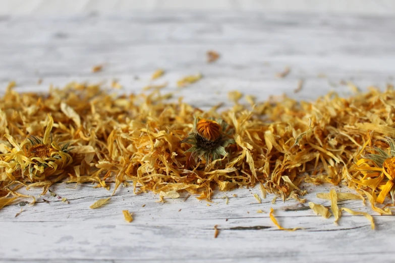 a pile of dried flowers sitting on top of a wooden table, a macro photograph, hurufiyya, close-up product photo, marigold, miniature product photo, dried leaves