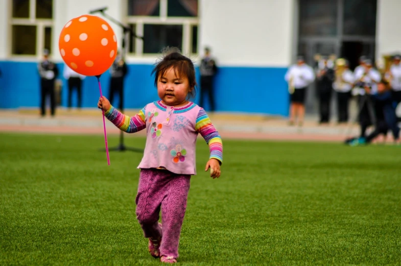 a little girl that is standing in the grass with a balloon, by An Zhengwen, flickr, on a football field, happy people, on the runway, square