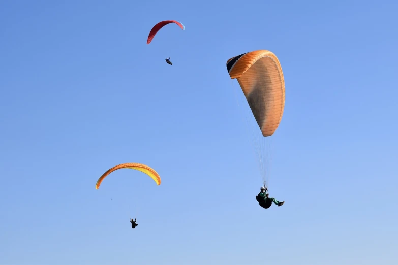 a couple of parachutes flying through a blue sky, a picture, figuration libre, trio, beautifully backlit, 7 0 mm photo