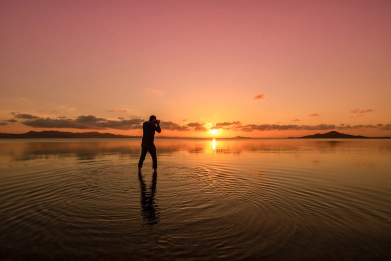 a person standing in a body of water at sunset, a picture, by Andrew Geddes, taking a picture, golden bay new zealand, camera photo, f/4