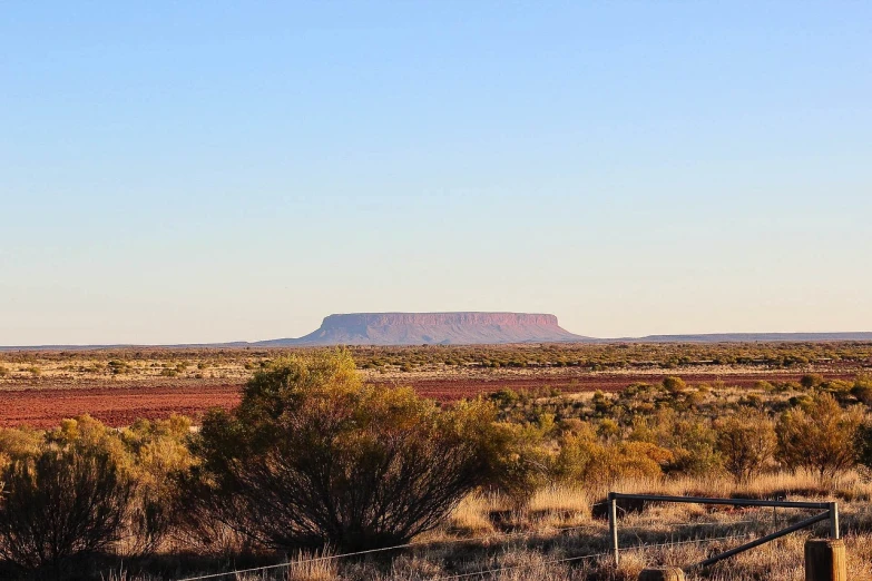 a fenced in area with a mountain in the distance, by Lee Loughridge, pexels, australian tonalism, red desert mars, 1128x191 resolution, visible from afar!!, big sharp rock