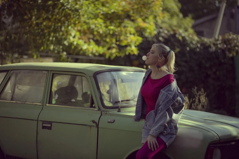 a woman sitting on the hood of a green car, a picture, inspired by Elsa Bleda, realism, bubble gum, moskvich, autumn season, blonde