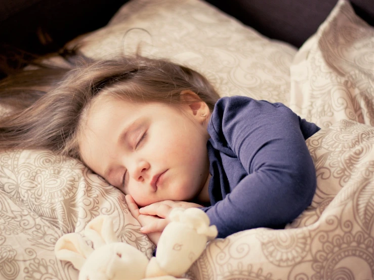 a little girl laying on top of a bed next to a stuffed animal, by Maksimilijan Vanka, pexels, he holds her while she sleeps, girl with brown hair, swirling around, subtle detailing