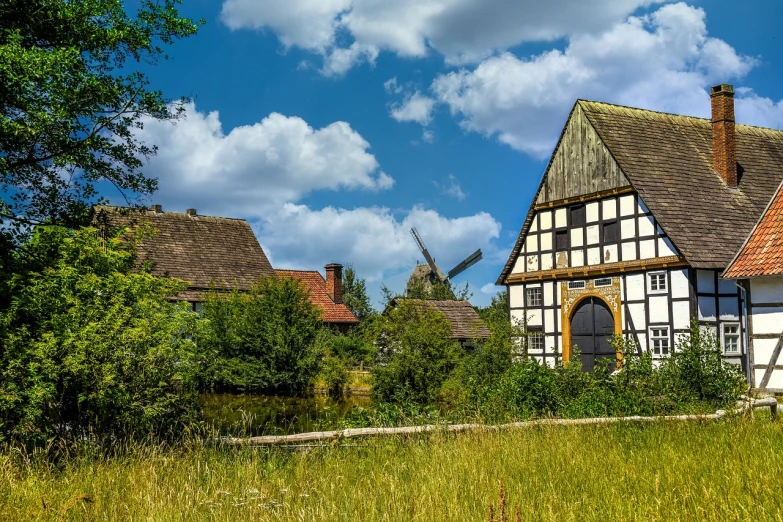 a house in a field with a windmill in the background, a picture, renaissance, hideen village in the forest, hannover, hot summer day, medieval architecture