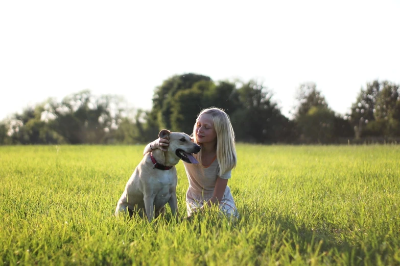 a woman kneeling in a field with a dog, gentle lighting, blonde, teenage girl, a green