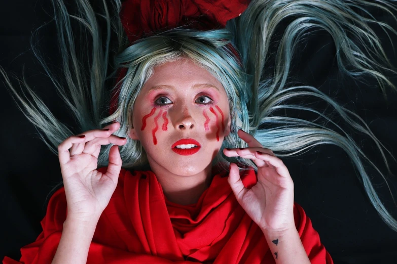 a woman with blue hair and red paint on her face, inspired by Cindy Sherman, die antwoord yolandi portrait, surreal tears from the moon, wearing a red outfit, cosplay photo