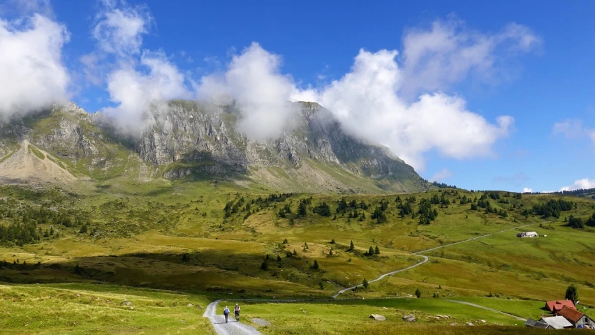 a group of people standing on top of a lush green hillside, by Werner Andermatt, flickr, les nabis, giant clouds, natural stone road, on a sunny day, limestone