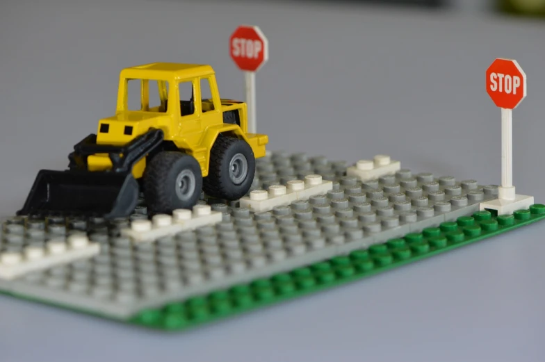 a toy bulldozer sitting next to a stop sign, inspired by Jan Kupecký, les automatistes, lego, flat roads, uncrop, 1 4 5 0