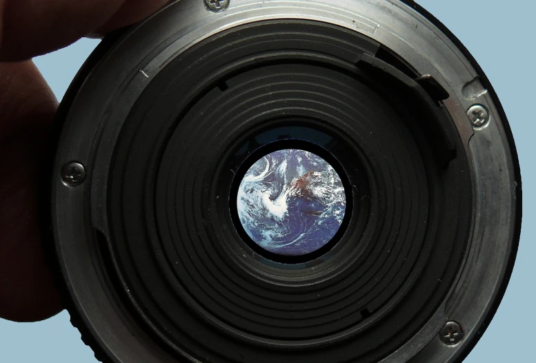 a close up of a person holding a camera lens, by Jon Coffelt, video art, earth in space, 8 k. filling of the view, back facing the camera, bottom angle