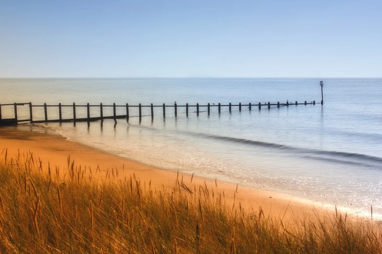 a pier sitting on top of a sandy beach next to the ocean, a photo, by Edward Corbett, shutterstock, reeds, summer morning, stock photo, uk