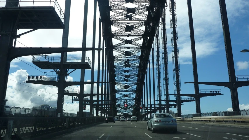 a car driving across a bridge on a sunny day, a picture, inspired by Sydney Carline, tumblr, huge support buttresses, view from inside, laquer and steel, tourist photo