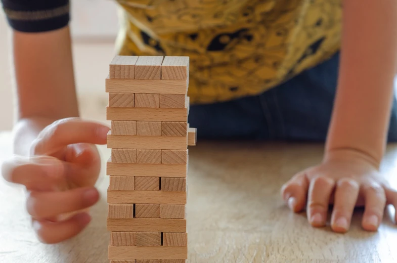 a child playing with wooden blocks on a table, a stock photo, by Jakob Gauermann, pexels, twisted giant tower, closeup of arms, videogame still, vertical portrait