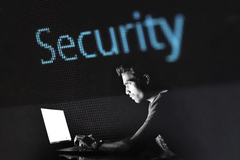 a man sitting in front of a laptop computer, by Mirko Rački, pixabay, security footage, neon signs in background, strong contrast, message