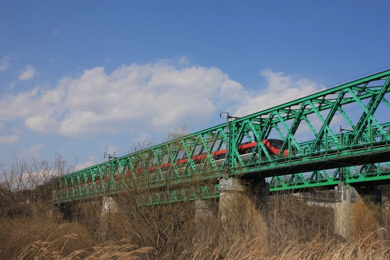 a green bridge with a red train going over it, flickr, sōsaku hanga, mechanical structure, blue sky, april, photo taken from far away