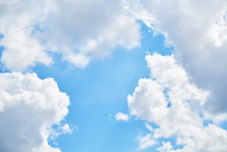 a plane flying through a cloudy blue sky, a stock photo, shutterstock, whorl. clouds, empty background, cotton candy clouds, on a bright day