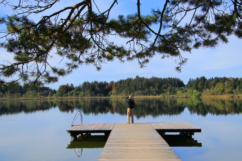 a person standing on a dock next to a body of water, a picture, by Istvan Banyai, shutterstock, arrendajo in avila pinewood, taking a picture, stock photo, belgium