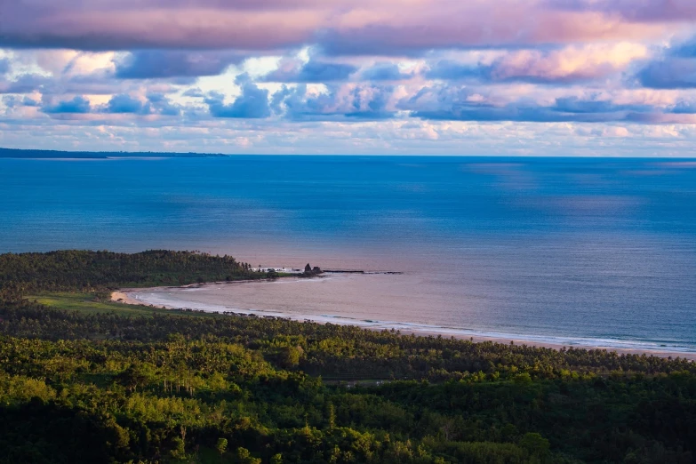 a large body of water sitting on top of a lush green hillside, by Raymond Normand, which shows a beach at sunset, hestiasula head, looking out at a pink ocean, wide aerial shot