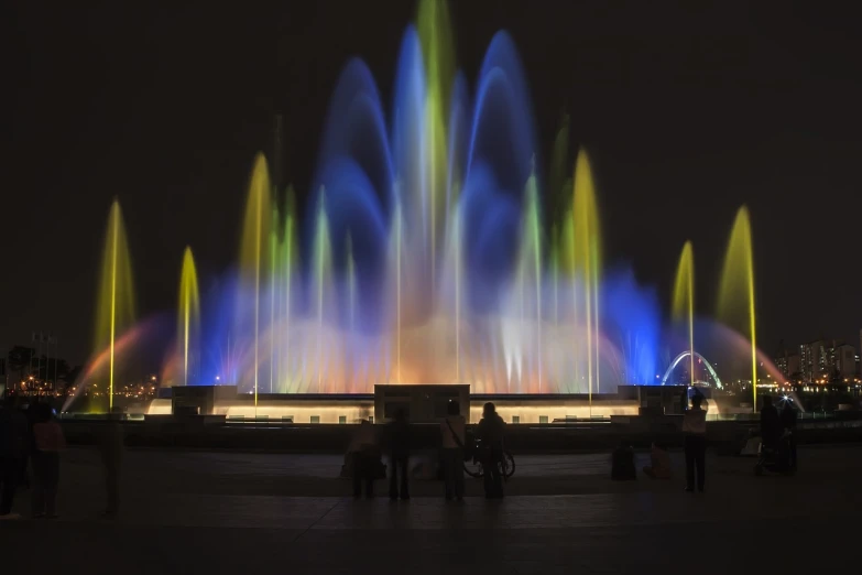 a group of people standing in front of a fountain, flickr, ethereal lighting colors scheme, a colorful, illuminated for rays of light, in barcelona