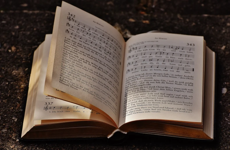 an open book sitting on top of a table, a photo, by Robin Guthrie, pixabay, baroque, singing for you, with notes, on the sidewalk, captured in low light