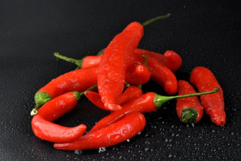 a pile of red hot peppers on a black surface, 3 4 5 3 1, silver red, drops, chalk