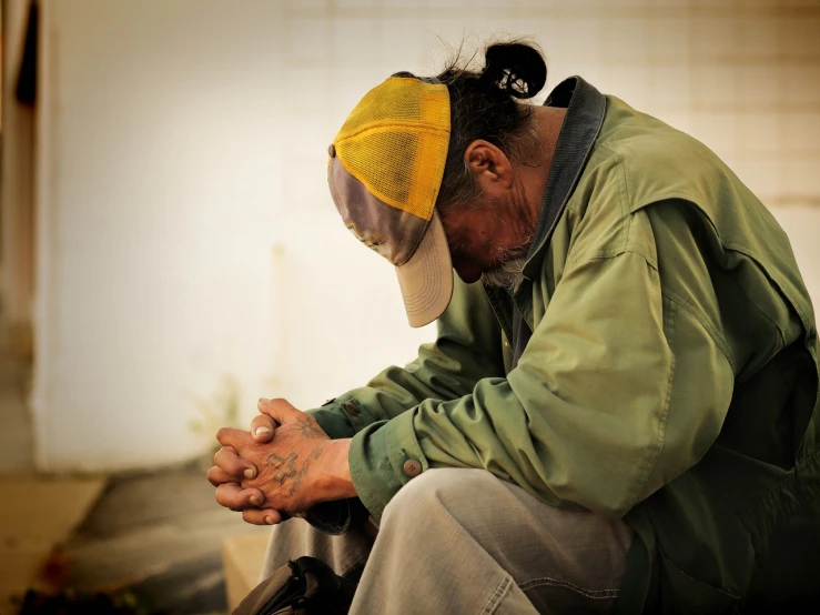 a man sitting on the ground with his head in his hands, by Paul Davis, flickr, danny trejo, japanesse farmer, doing a prayer, cyberpunk homeless