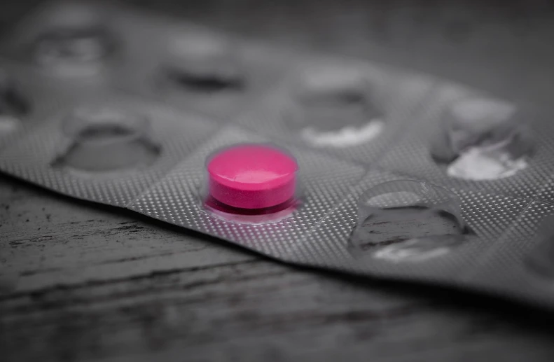 a pink pill sitting on top of a blister pack, a picture, by Amelia Peláez, pexels, selective color effect, stock photo