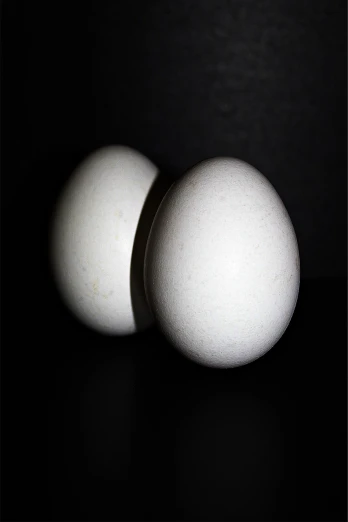 two eggs sitting next to each other on a table, inspired by Robert Mapplethorpe, flickr, standing with a black background, back - lit, [ closeup ]!!, white eclipse