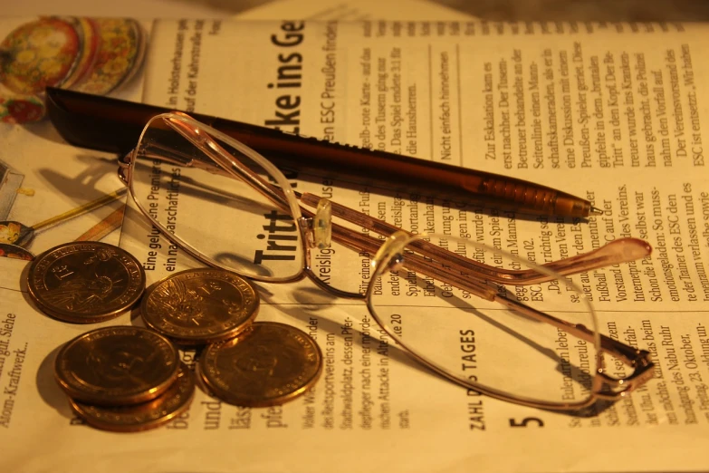 a pair of glasses sitting on top of a newspaper, by Alfons von Czibulka, coins, golden glow, study, unedited