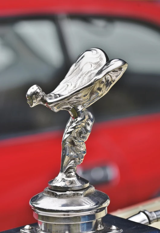 a close up of a hood ornament on a car, an art deco sculpture, by Raymond Normand, pixabay, art nouveau, with depth of field, in style of chrome hearts, red car, winged victory of samothrace
