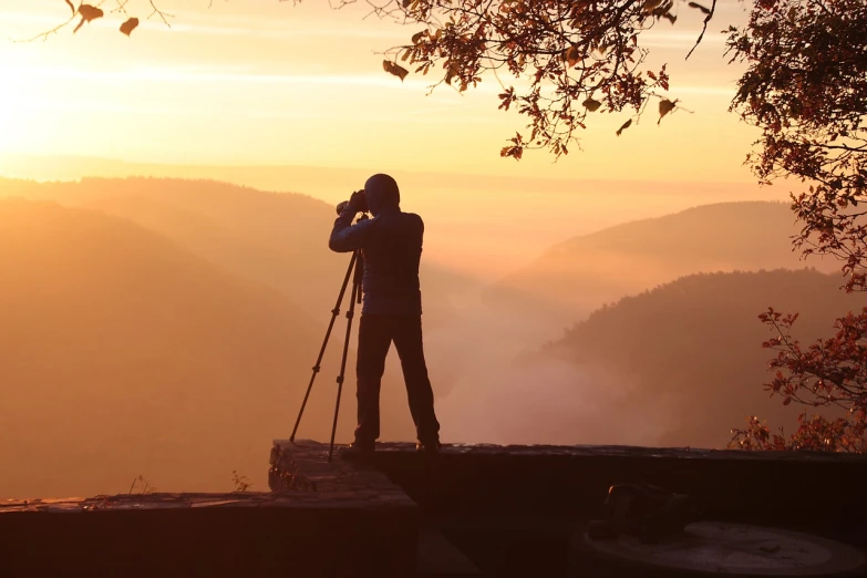 a man standing on top of a mountain holding a camera, a picture, art photography, sunrise lighting, photograph captured in a forest, istockphoto, looking over west virginia