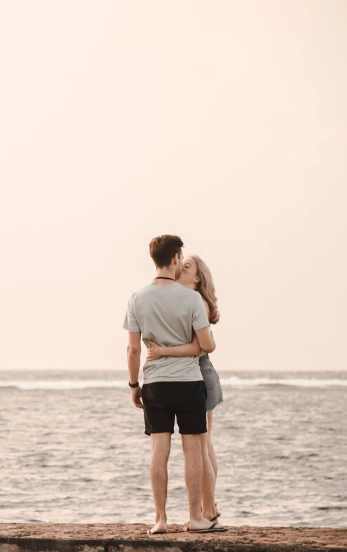 a man and a woman standing on a pier next to the ocean, a picture, by Emma Andijewska, kissing, bali, background image, on the sand