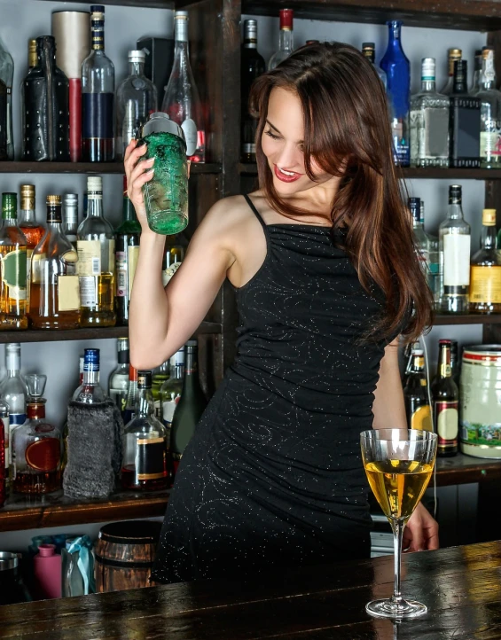 a woman in a black dress holding a bottle of alcohol, a portrait, pexels, bartending, petite girl, absinthe, looking happy