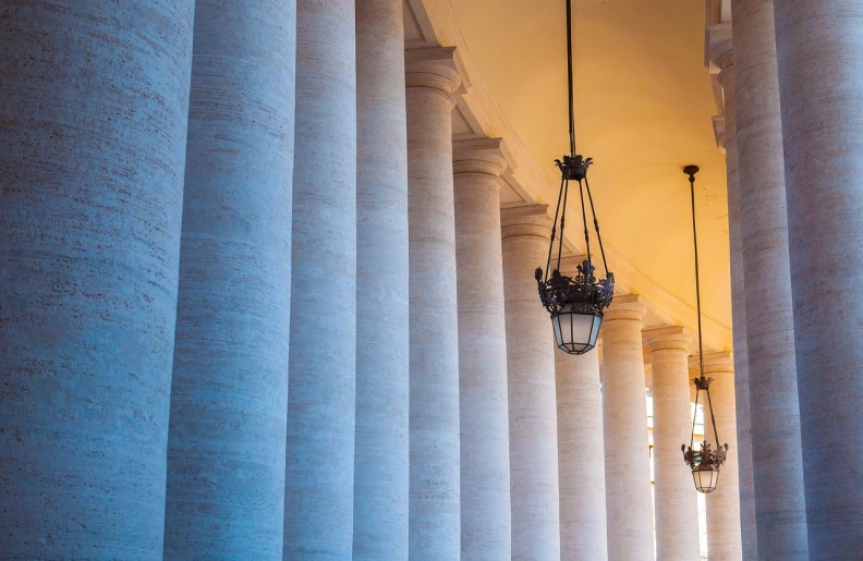 a group of lamps hanging from the ceiling of a building, a photo, inspired by Hubert Robert, shutterstock, neoclassicism, colonnade, vatican in background, architecture photo, curved perspective