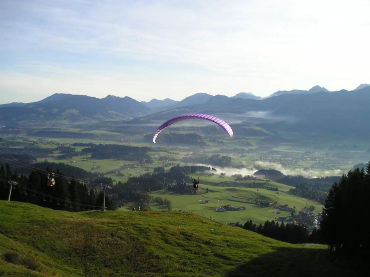a paraglider flying over a lush green hillside, a picture, by Juergen von Huendeberg, flickr, happening, on flickr in 2 0 0 3, early morning, with mountains in the distance, lovely valley