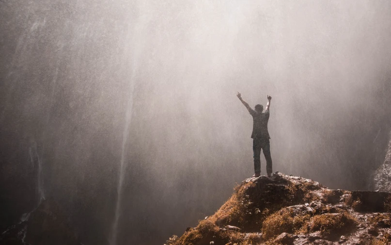 a person standing in front of a waterfall, pexels contest winner, figuration libre, arms held high in triumph, fog and dirt, screensaver, heaven in the top